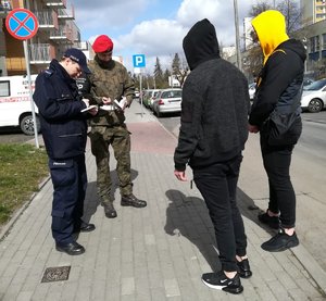 policjant i żandarm legitymują dwójkę osób w kapturach