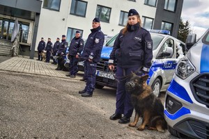 Policjantka z psem przy radiowozie.