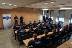 Dwóch policjantów stoi na przeciwko siedzącym w ławkach uczestnikom kursu aspiranckiego