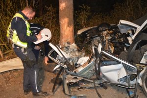 Policjanci  dokonujący oględzin miejsca wypadku. Obaj przy rozbitym aucie.