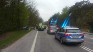 obraz miejsca zdarzenia, gdzie na pierwszym planie są służby. Dwa radiowozy policji, karetka i Straż Pożarna.