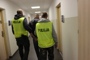 Podejrzany wraz z policjantami idą korytarzem komendy.