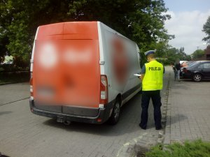 Policjant wykonuje oględziny tyłu pojazdu, który potrącił kobietę.