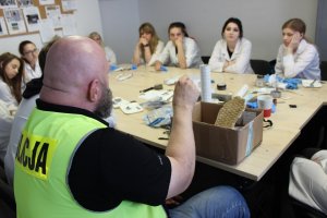 Policjant na tle zabezpieczonego śladu obuwia , wokół studenci Wydziału Chemii.