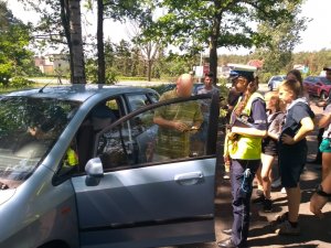 kierowca i policjantka przy kontrolowanym samochodzie. W tle dzieci