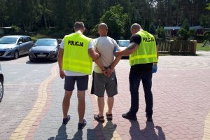 policjanci prowadzą zatrzymanego, który jest zakuty w kajdanki