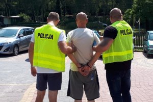 policjanci prowadzą zatrzymanego, który jest zakuty w kajdanki