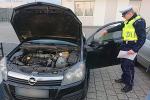 policjant kontroluje auto na parkingu przed komisariatem