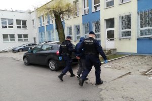 Policjanci prowadzą podejrzanego do komisariatu i pokoju przesłuchań.