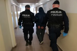 Policjanci prowadzą podejrzanego do komisariatu i pokoju przesłuchań.