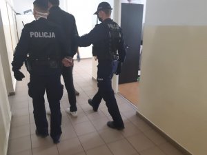 policjanci prowadza zatrzymanego wandala do zniszczenia pomnika Jana Pawła II