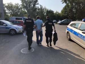 Policjanci z patrolu z Komisariatu Policji  prowadzący sprawcę kradzieży zuchwałej najpierw po korytarzu komisariatu a następnie po parkingu aż do radiowozu.