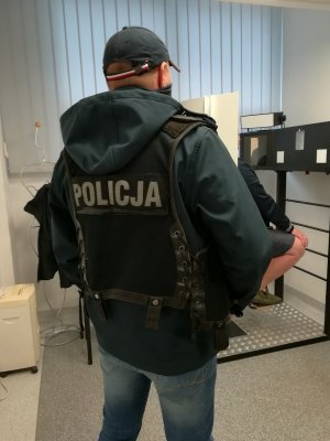 Policjant wydziału kryminalnego Komisariatu Policji Toruń Śródmieście pilnujący podejrzanego o posiadanie znacznej ilości narkotyków podczas wykonywania zdjęcia sygnalitycznego.