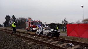 Zdjęcie z miejsca śmiertelnego wypadku w Papowie Toruńskim . Na zdjęciu widoczni policjanci z Wydziału Ruchu Drogowego Komendy Miejskiej Policji w Toruniu,  wykonujący czynności na miejscu zdarzenia, zniszczony  pojazd marki ford focus i szynobus wraz z podpiętymi wagonami. Przód szynobusa zniszczony w skutek zderzenia