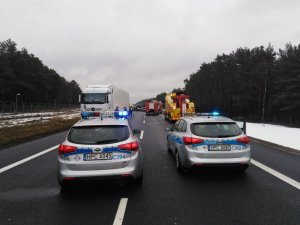 na pierwszym planie dwa policyjne radiowozy na drodze, w tle rozbite samochody