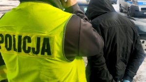 policjanci w żółtych kamizelkach odblaskowych prowadzą podejrzanego