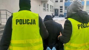 policjanci w żółtych kamizelkach odblaskowych prowadzą podejrzanego