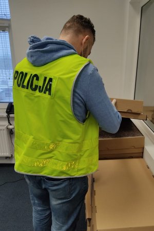 policjant w kamizelce odblaskowej odwrócony tyłem, w tle kartony z papierosami