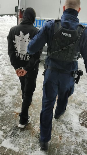 Policjanci w umundurowaniu służbowym prowadzą podejrzanych do radiowozu.