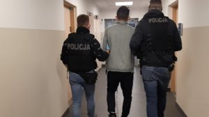 Dwóch policjantów prowadzi zatrzymanego  korytarzem komendy.