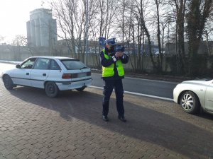 kontrola drogowa, policjant z laserowym miernikiem prędkości dokonuje pomiaru, w tle radiowóz