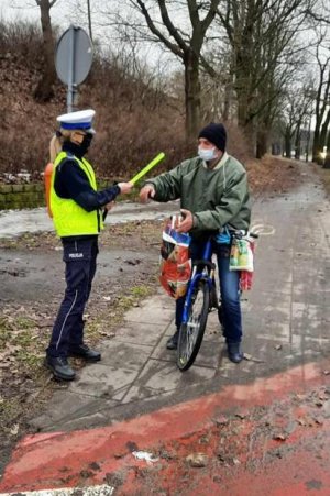 Policjantka  podczas akcji Niechroniony Uczestnik Ruchu Drogowego wręcza  rowerzyście opaskę odblaskową.