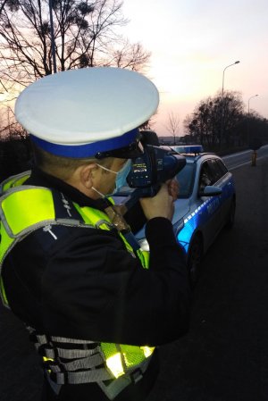 Zdjęcia wieczorem i nocą policjanta podczas działań na drodze krajowej numer 91. Policjant w kamizelce i z ręcznym miernikiem prędkości.