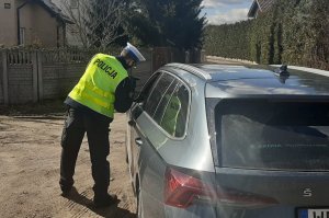 Policjant z ręcznym miernikiem prędkości przy drodze kontrolujący szybkość jazdy pojazdami oraz pokazujący kierowcy jego wynik.