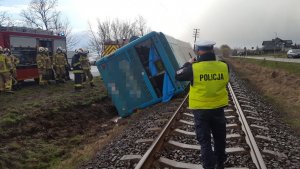 Zdjęcie autobusu przewróconego częściowo w rowie,  dachem  zalegającego na torowisku. Na miejscu pracujące służby : Policja i Straż Pożarna.