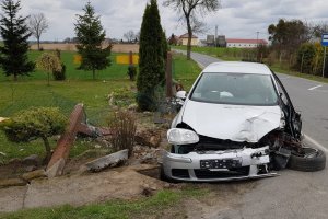 Zdjęcie z miejsca kolizji w Brzezinku. volkswagen  w kolorze białym z uszkodzonym przodem pojazdu i przednim nadkolem od strony kierowcy jak również leżącym przy nim kołem.