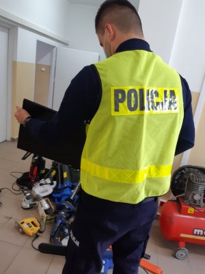 Policjant rozpakowuje i układa  przedmioty  odzyskana do sprawy włamań do altanek.