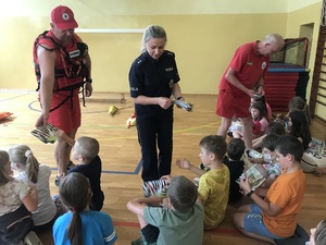Policjantka i ratownicy przekazują dzieciom książeczki nt. bezpiecznego spędzania wolnego czasu oraz ulotki nt. bezpieczeństwa nad wodą.