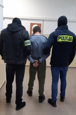 Sprawca  włamań do pojazdów prowadzony przez policjantów   kryminalnych  korytarzem do pokoju przesłuchań.