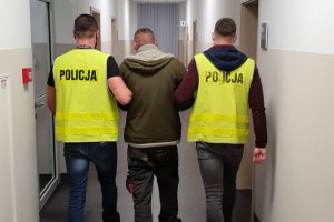 policjanci w kamizelkach odblaskowych prowadzą podejrzanego