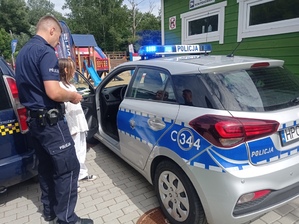 Policjant prezentuje dziewczynce oznakowany radiowóz