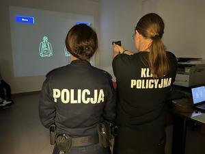 Uczennica w towarzystwie policjantki ćwiczy strzelanie na laserowym trenażerze