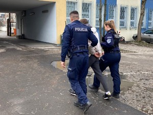 Dwóch policjantów prowadzi mężczyznę z kajdankami na rękach