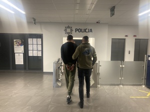 policjant prowadzi mężczyznę z kajdankami na rękach