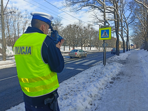 policjant w mundurze trzyma w dłoni miernik prędkości skierowany na jezdnię