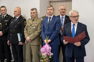 na sali stoją mundurowi i osoby w ubraniach cywilnych