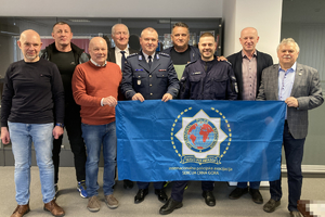 mężczyźni stoją na tle flagi organizacji ipa, w tym umundurowani policjanci