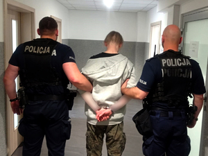 dwóch umundurowanych policjantów prowadzi zatrzymanego mężczyznę korytarzami komisariatu