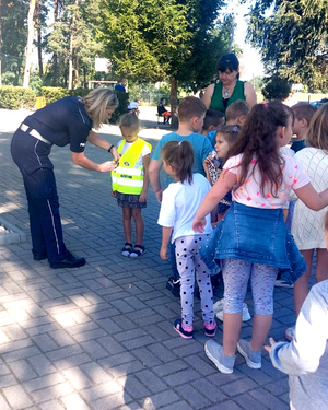 policjantka ubiera dzieci w kamizelki odblaskowe