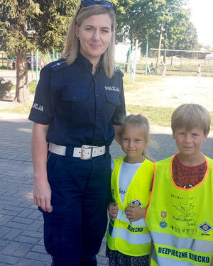 pamiątkowe zdjęcie policjantki i dzieci w kamizelkach odblaskowych