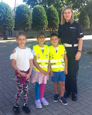 pamiątkowe zdjęcie policjantki i dzieci w kamizelkach odblaskowych