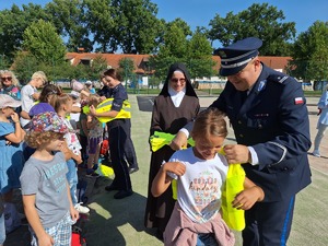 Komendant Miejski pomaga zakładać kamizelkę odblaskową dziecku