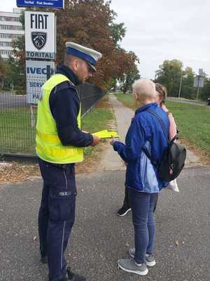 Policjant przekazuje elementy odblaskowe przechodniom