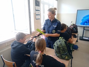 Policjantka przekazuje uczniom elementy odblaskowe