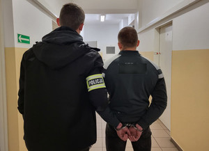 Policjant prowadzi korytarzem zatrzymanego