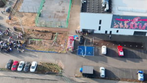 ujęcie z drona. Widać wóz strażacki oraz radiowóz policji. W tle ewakuacja dzieci z budynku szkoły